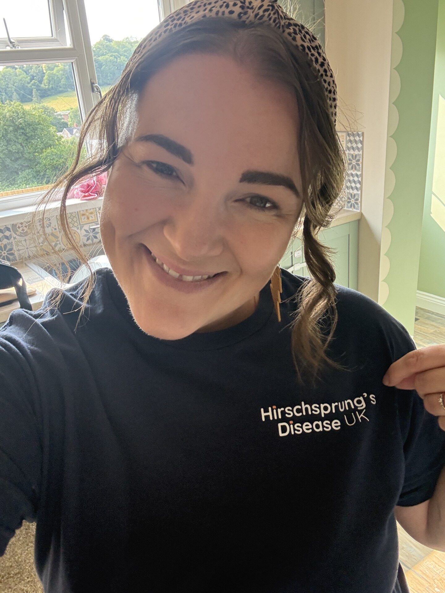 A woman smiling at the camera, pointing to the logo on her t-shirt that reads 