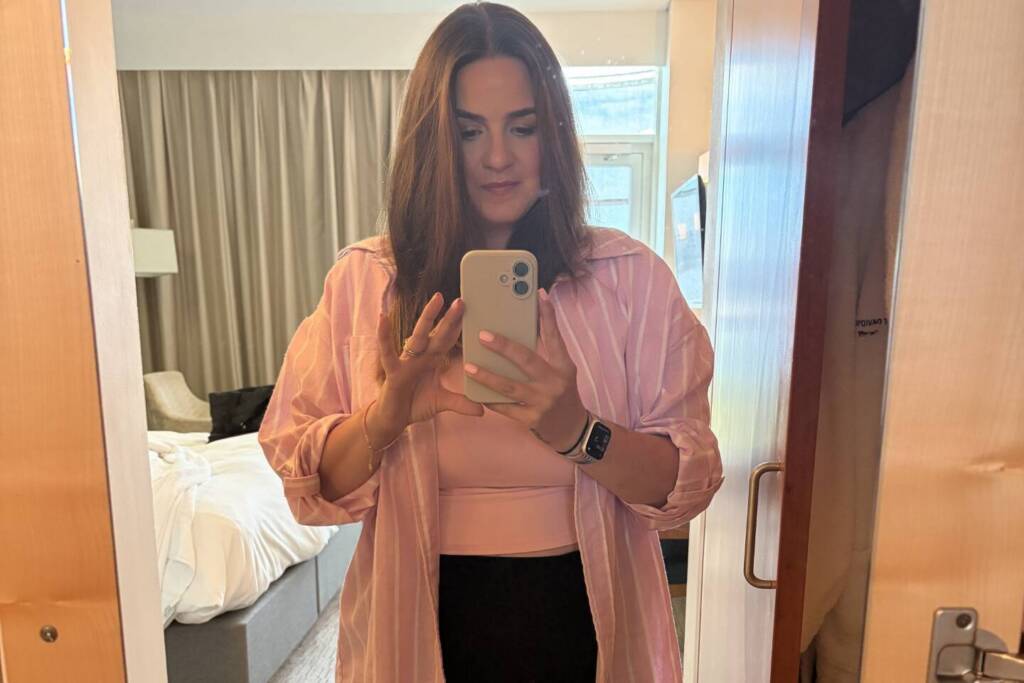  A woman wearing a pink jump and black trousers take a photo in front of a full-length mirror