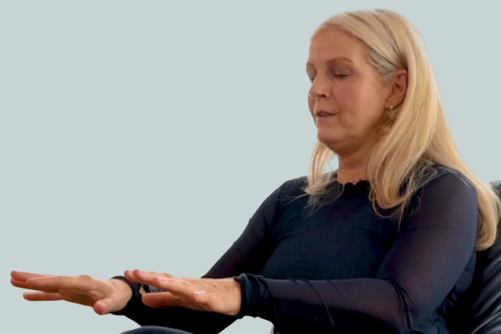 A blonde woman holds out her hands and looks at them