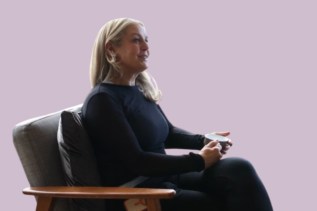 A blonde women sits in a chair, smiling