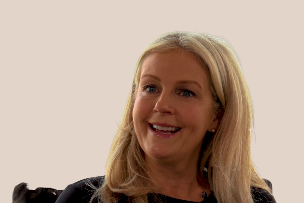 A blonde woman in a black top smiles at the camera.