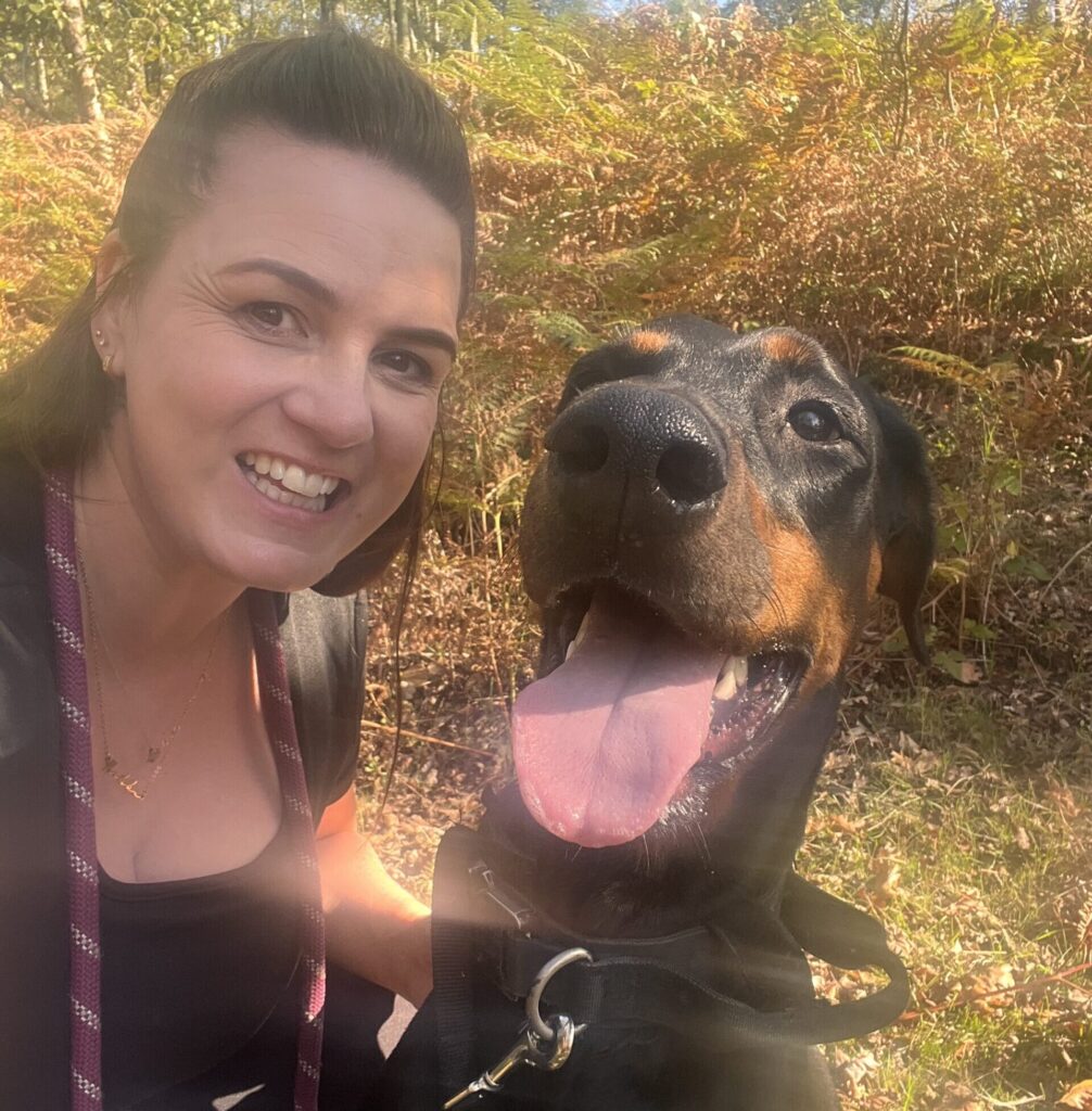 A woman and a dog both smile for a picture out in nature