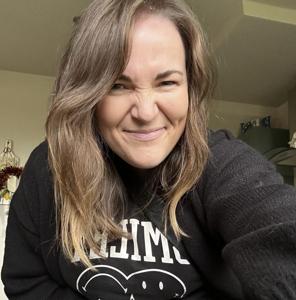 A brown-haired woman looks down and smiles while sat in a green room