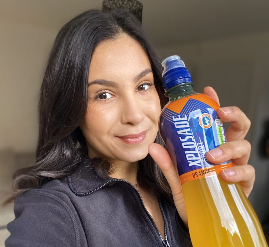 A dark-haired woman holds up a lucozade