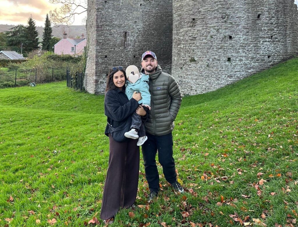 A man and a woman hold a baby in front of a castle