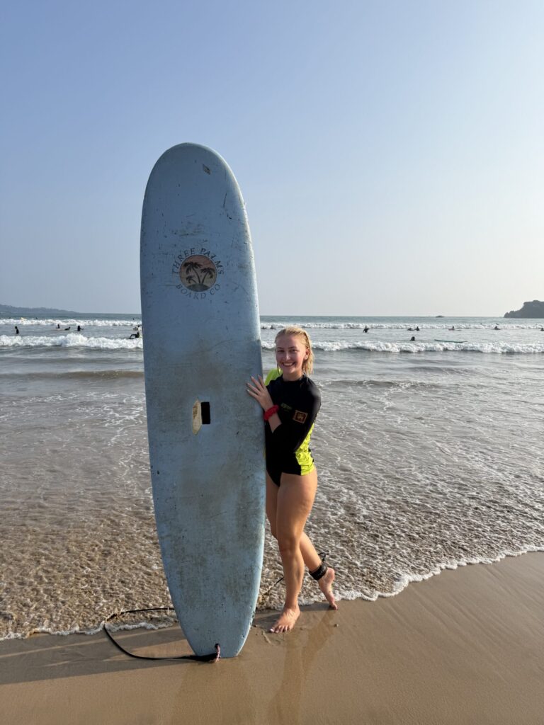 A woman in a wetsuits holds up a surfboard at the beach