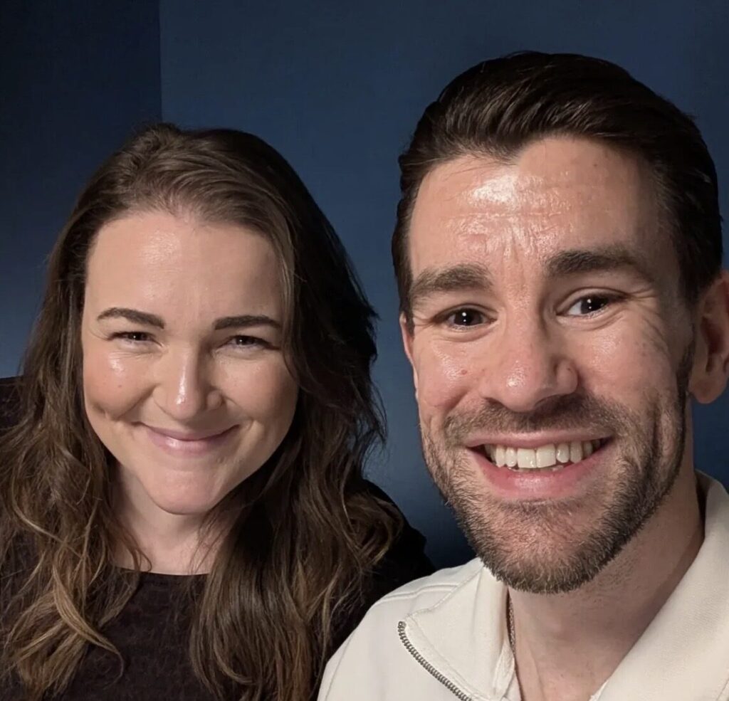 A man and a woman sit next to each other in a dark room and smile