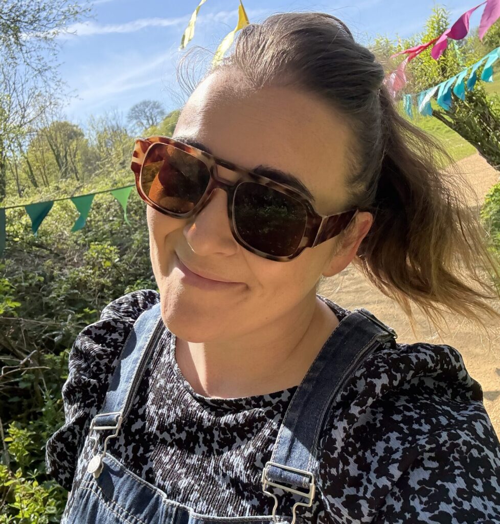 A woman in sunglass smiles as she walks outdoors in the sunshine
