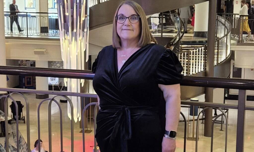A woman in a black dress stands in front of a railing