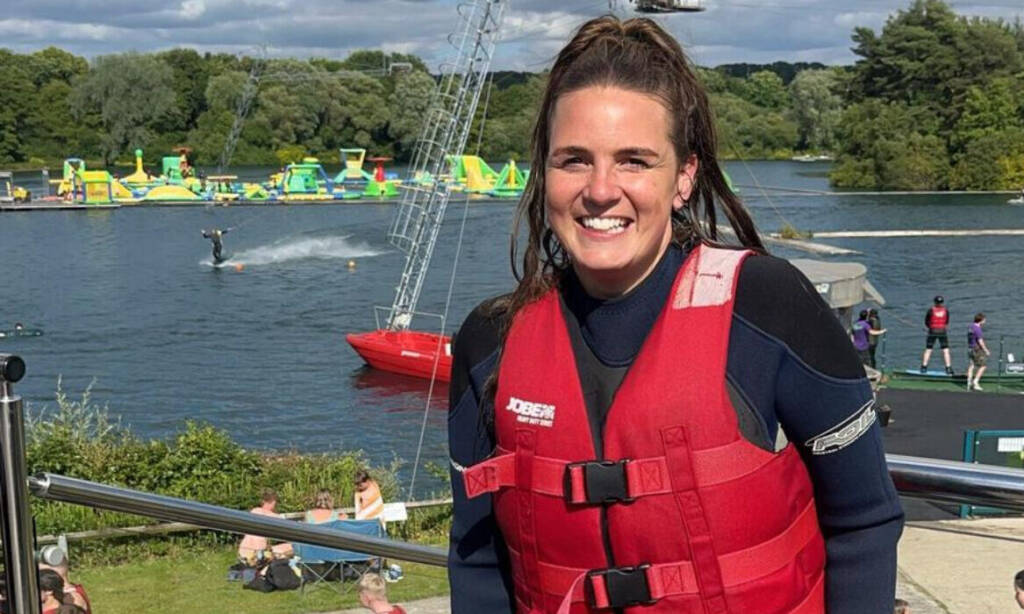 A woman wearing a life jacket smiles in front of a lake before going in the water.
