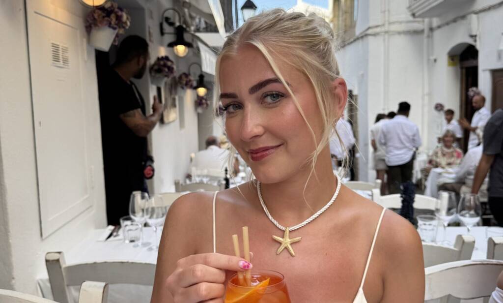 A woman poses in a white dress holding an orange cocktail