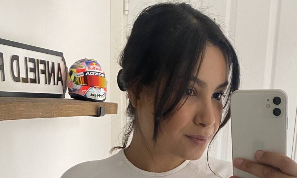 A woman takes a selfie in a white t-shirt with her stoma bag showing
