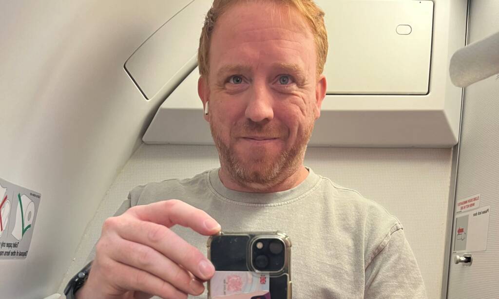 A red-haired man takes a photo of his ostomy bag in an aeroplane bathroom