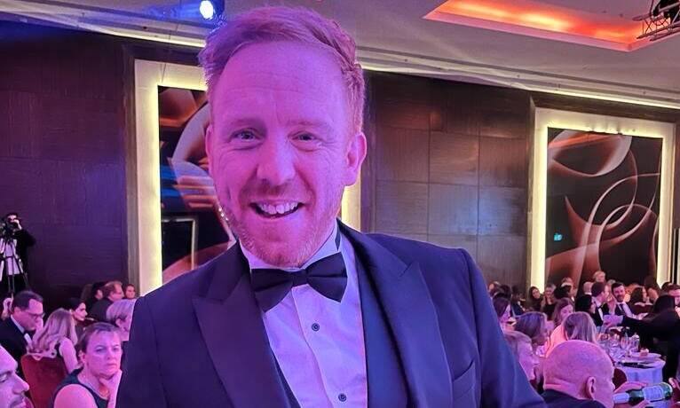A read-haired men poses in a tuxedo at an awards event